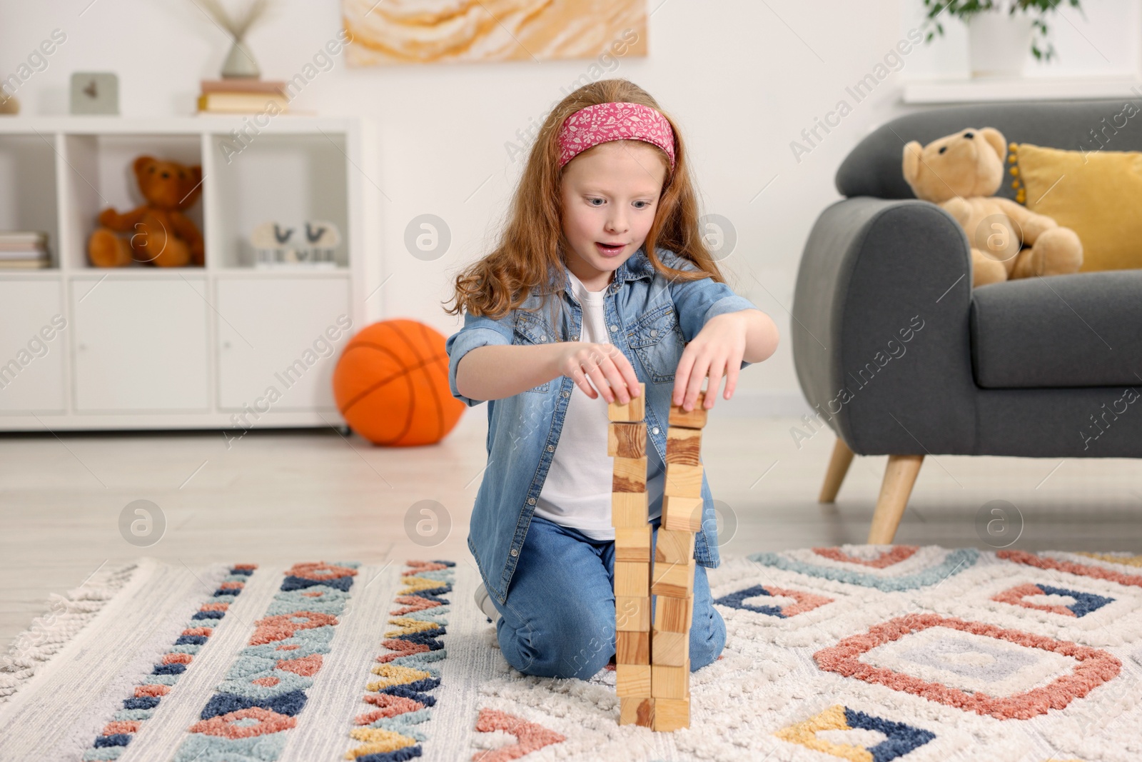 Photo of Little girl building towers with wooden cubes on floor indoors