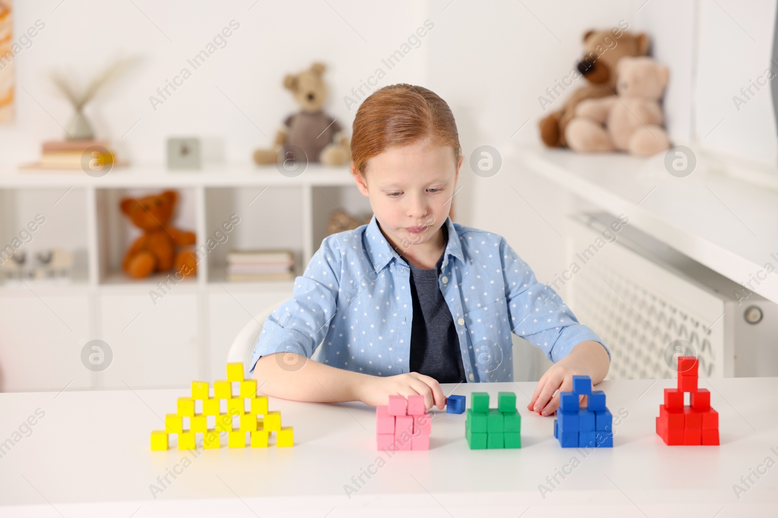 Photo of Little girl playing with colorful cubes at white table indoors