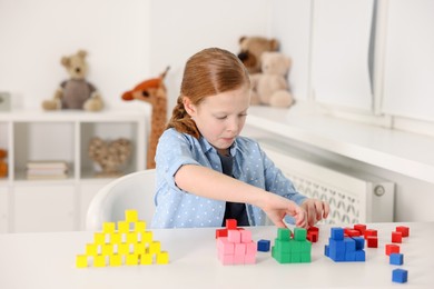 Photo of Little girl playing with colorful cubes at white table indoors