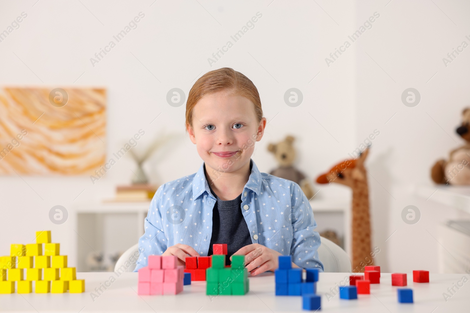 Photo of Little girl playing with colorful cubes at white table indoors