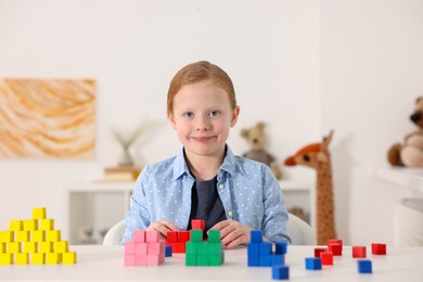 Photo of Little girl playing with colorful cubes at white table indoors