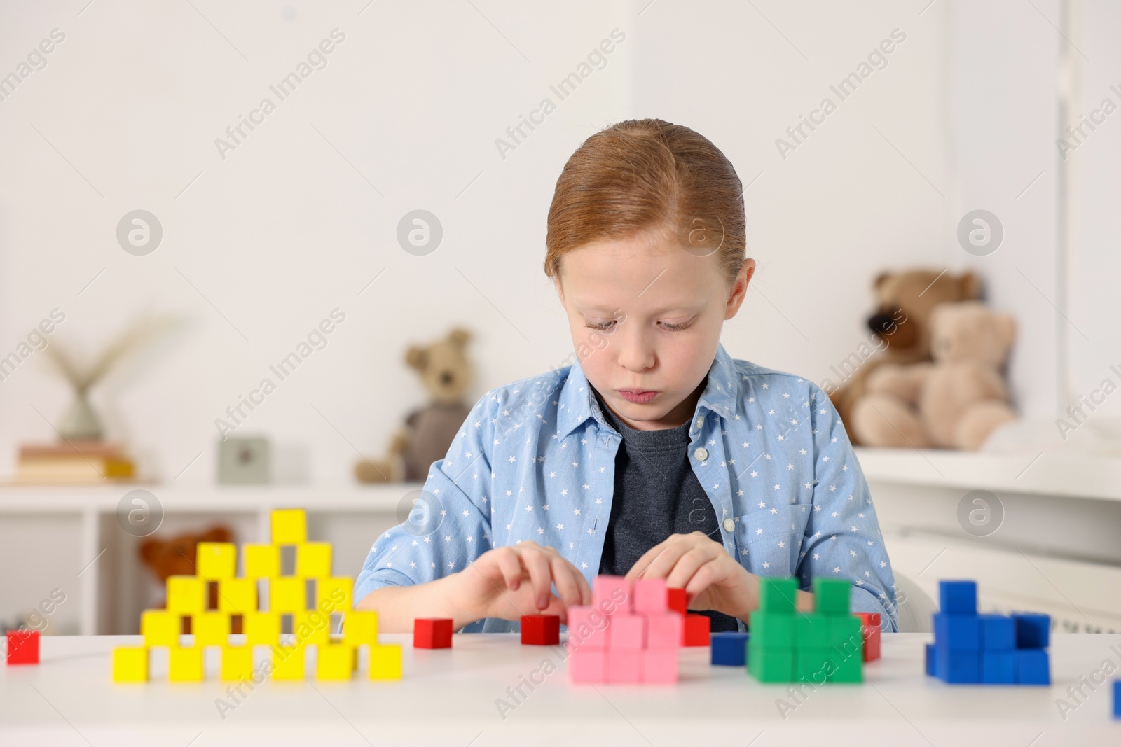 Photo of Little girl playing with colorful cubes at white table indoors