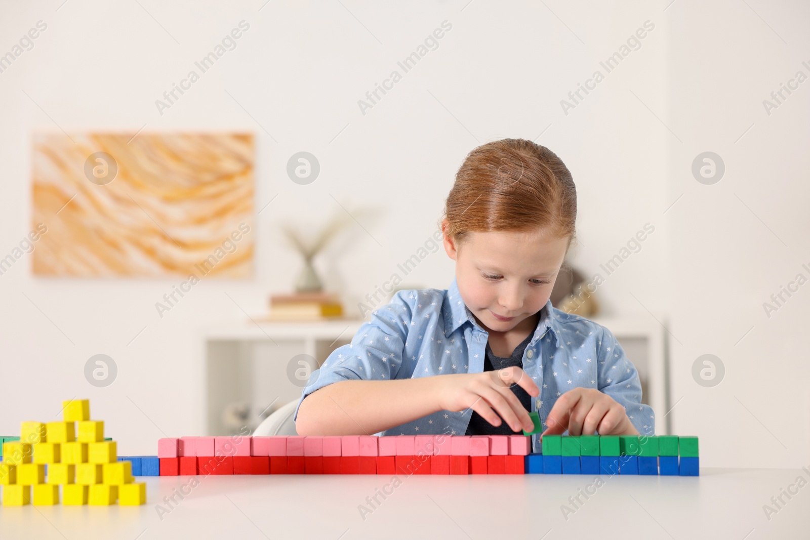 Photo of Little girl playing with colorful cubes at white table indoors