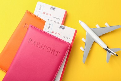 Photo of Passports in color covers, plane model and flight tickets on yellow background, top view