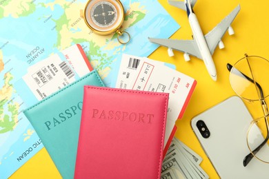 Photo of Passports with tickets, map, money, compass, smartphone, glasses and airplane model on yellow background, flat lay