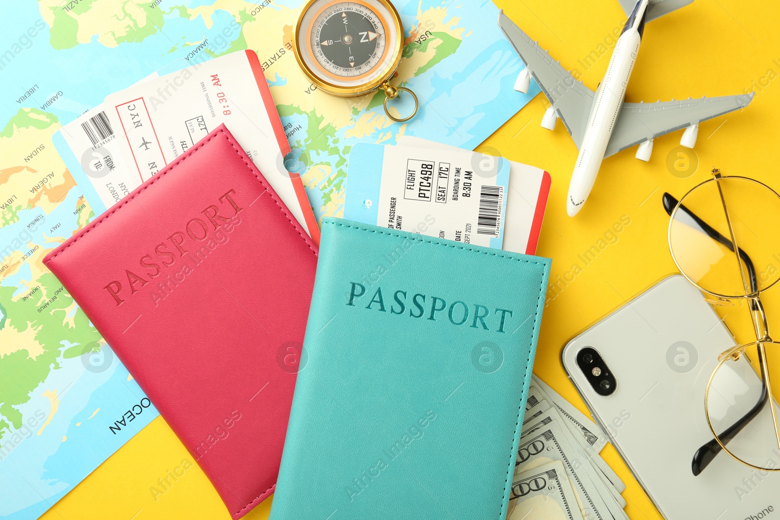 Photo of Passports with tickets, map, money, compass, smartphone, glasses and airplane model on yellow background, flat lay