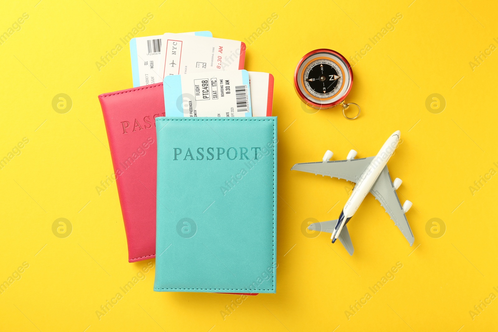 Photo of Passports with tickets, compass and airplane model on yellow background, flat lay