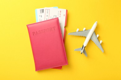 Photo of Passport with tickets and airplane model on yellow background, top view