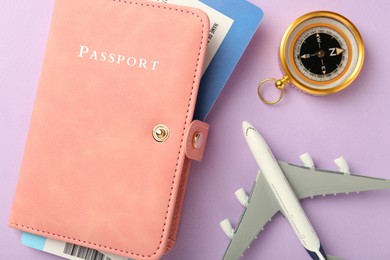 Photo of Passport with tickets, compass and airplane model on lilac background, flat lay