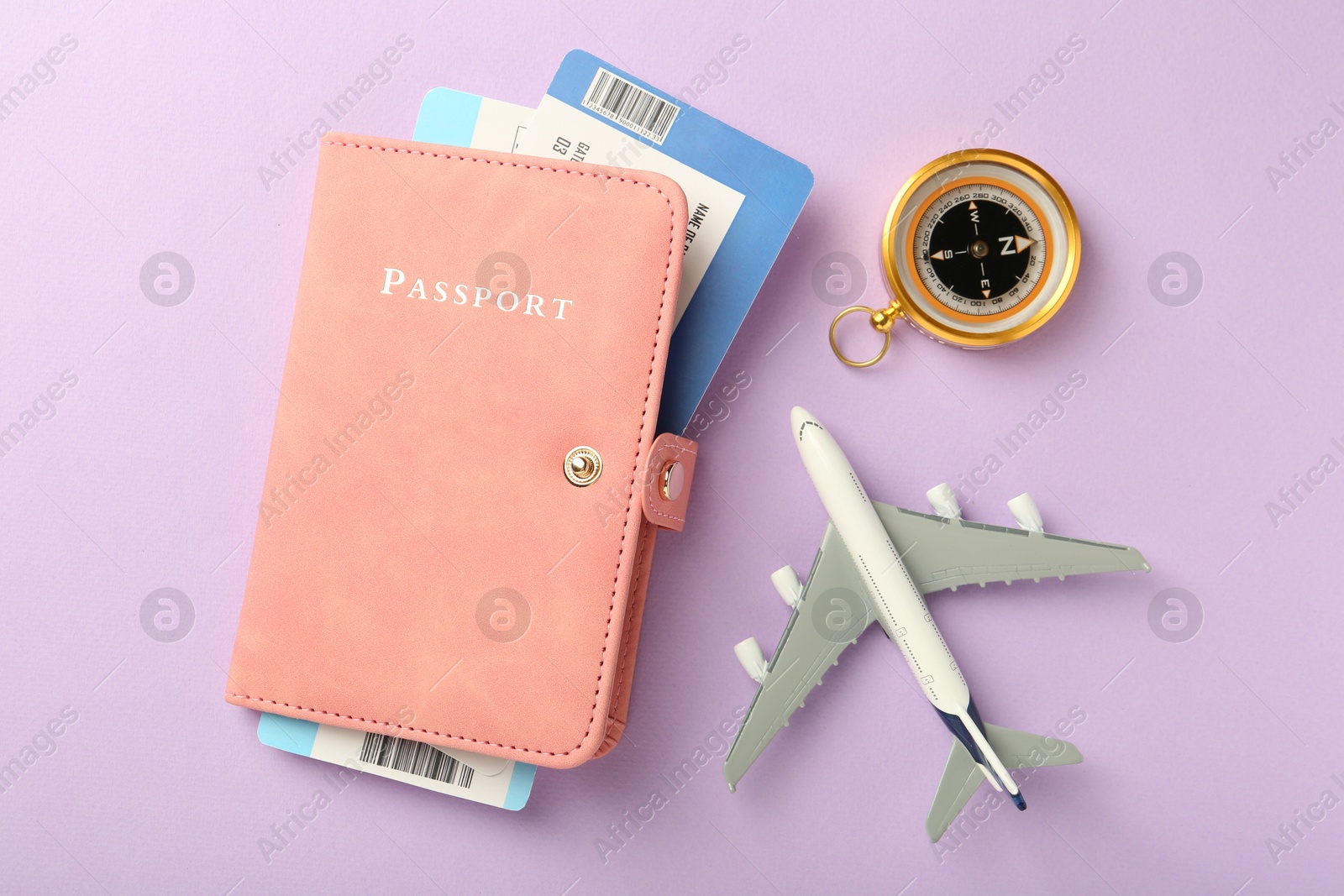 Photo of Passport with tickets, compass and airplane model on lilac background, flat lay