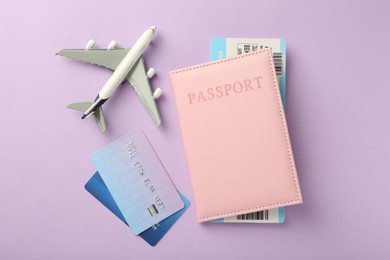 Photo of Passport with ticket, credit cards and airplane model on lilac background, flat lay