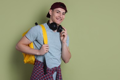 Photo of Student with headphones and backpack on olive background, space for text