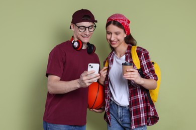 Photo of Student showing something on smartphone to girl against olive background