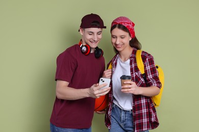 Photo of Student showing something on smartphone to girl against olive background