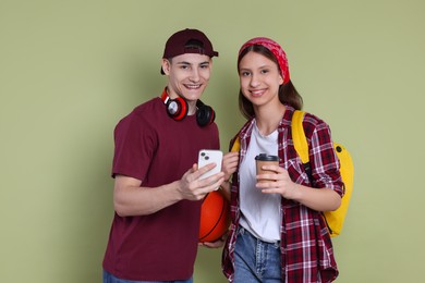 Photo of Student showing something on smartphone to girl against olive background