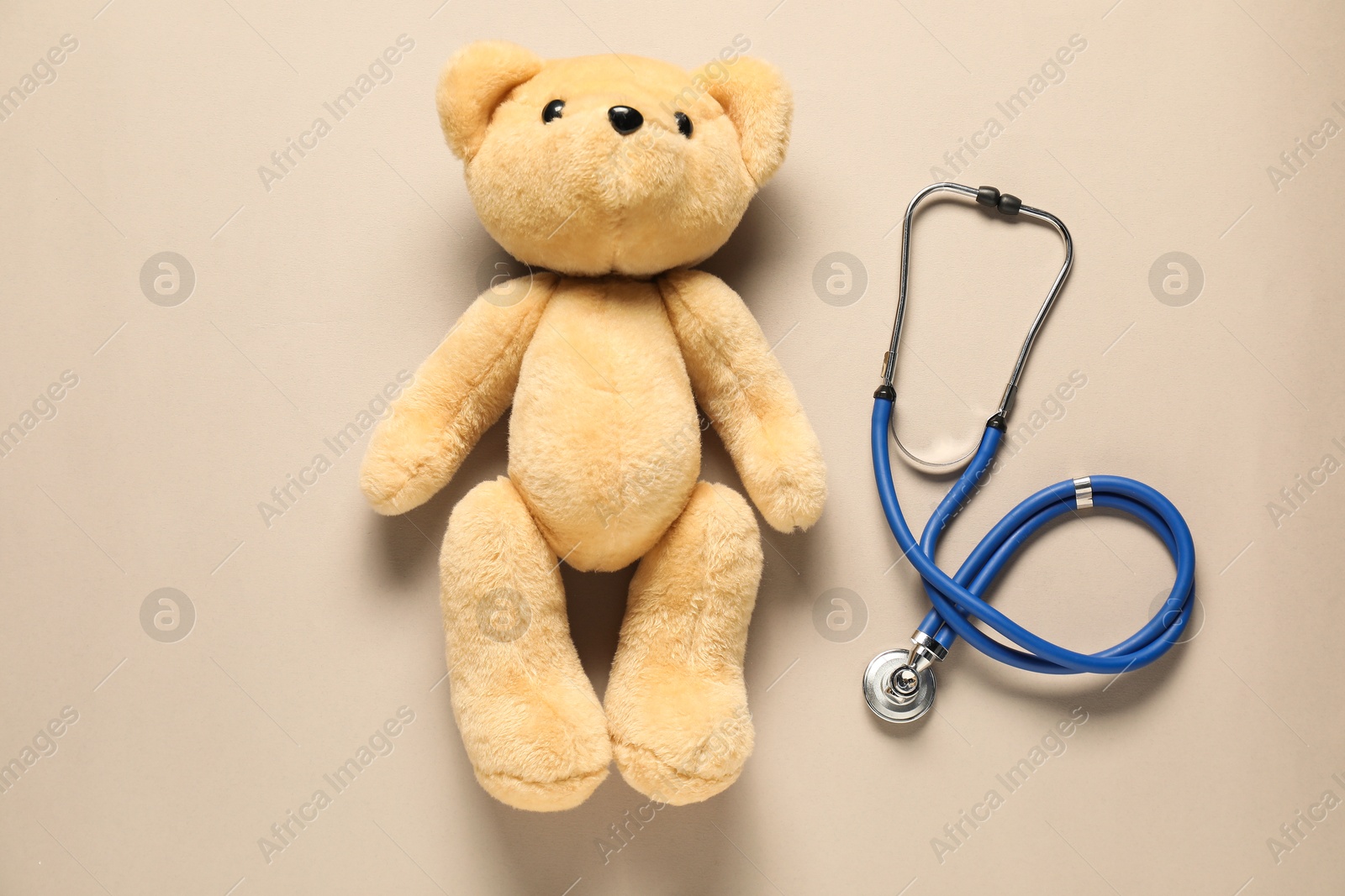 Photo of Pediatrics concept. Teddy bear with stethoscope on beige background, top view