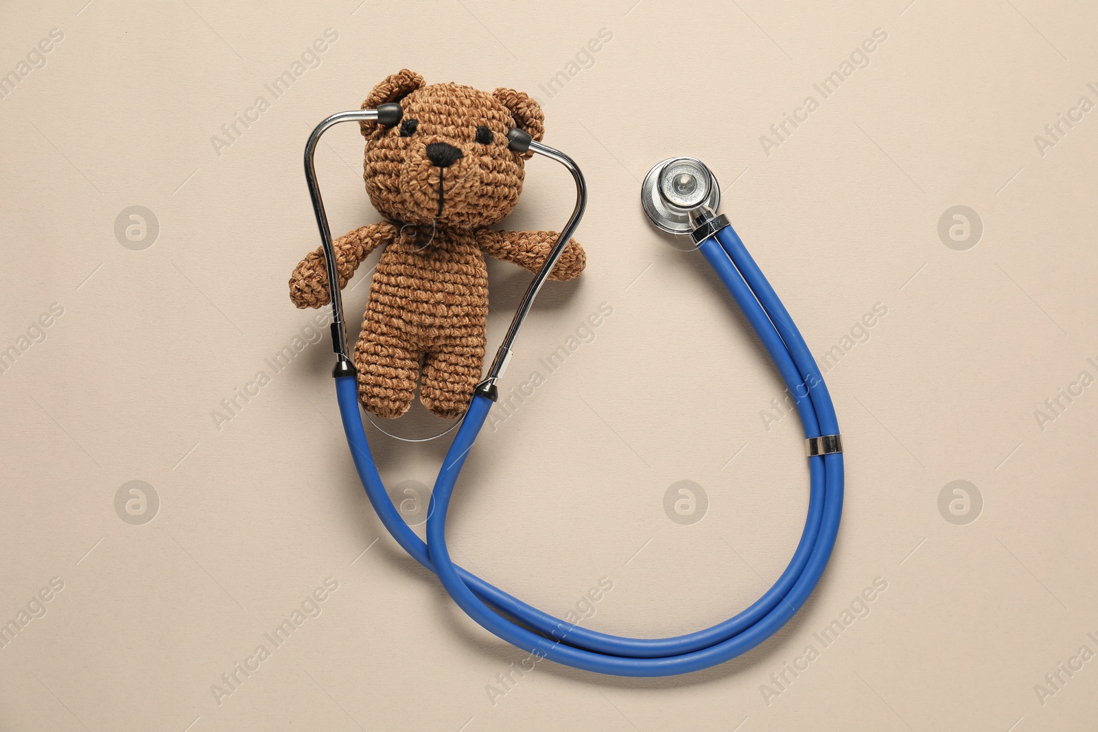 Photo of Pediatrics concept. Toy bear with stethoscope on beige background, top view