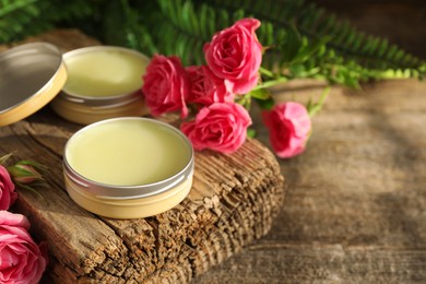 Photo of Natural solid perfume and pink roses on wooden table, space for text