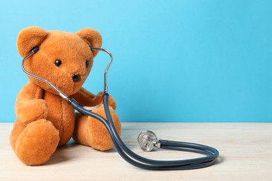 Photo of Pediatrics concept. Teddy bear with stethoscope on wooden table against light blue background, space for text