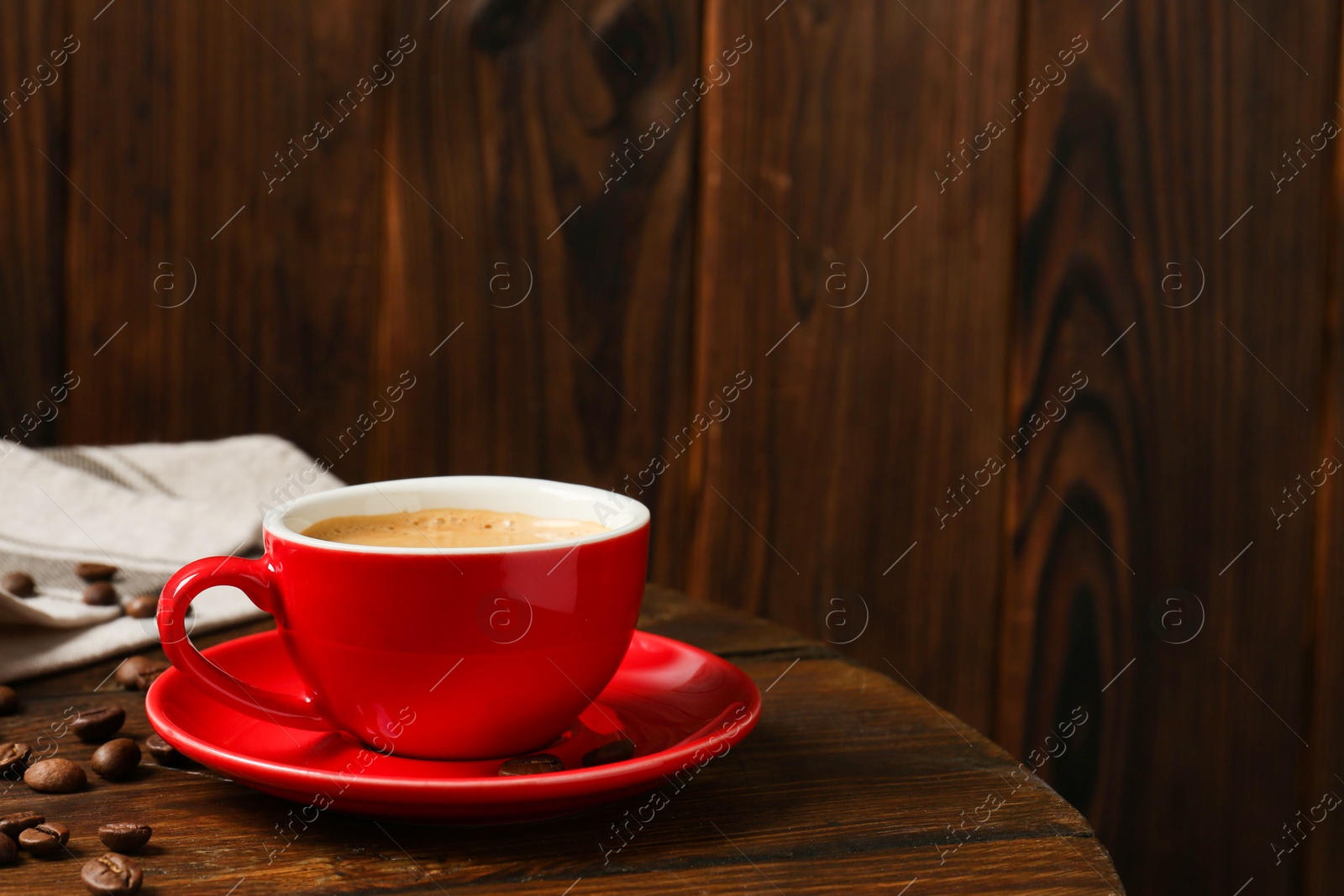 Red cup with coffee and roasted beans on wooden table, space for text Photo of Red cup with coffee and roasted beans on wooden table, space for text