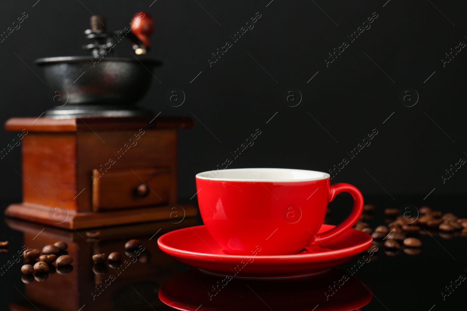 Red cup with coffee, vintage grinder and roasted beans on black background Photo of Red cup with coffee, vintage grinder and roasted beans on black background