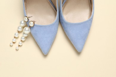 Photo of Stylish shoes and pearl earrings on beige background, top view