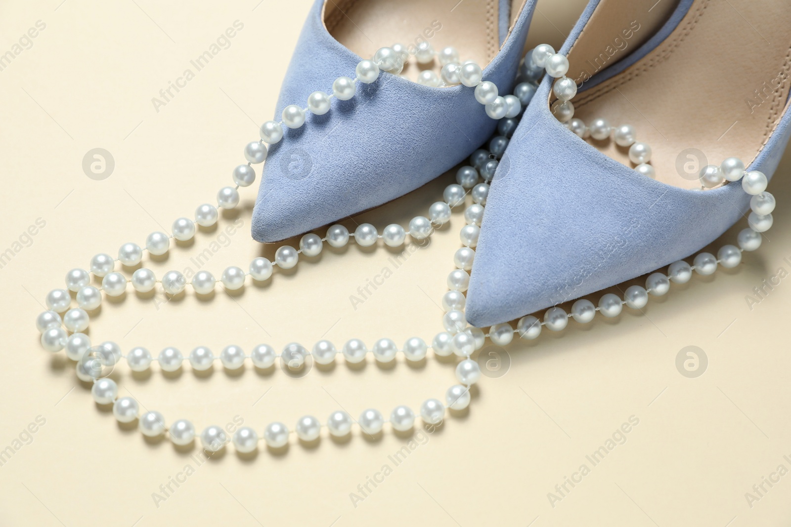 Photo of Stylish shoes and pearl necklace on beige background, closeup