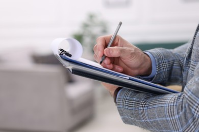 Photo of Real estate appraisal. Inspector with clipboard conducting property valuation indoors, closeup. Space for text