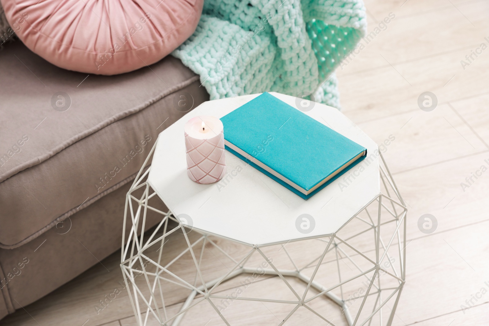 Photo of Stylish coffee table with book and candle near sofa at home, closeup