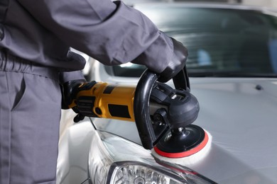 Photo of Man polishing car hood with orbital polisher indoors, closeup