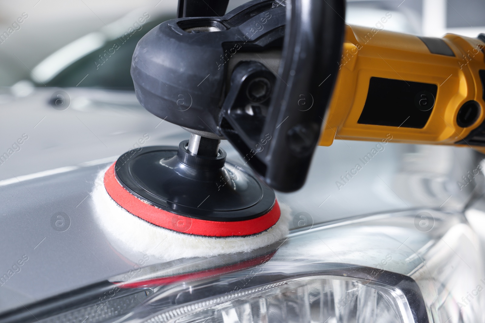 Photo of Man polishing car hood with orbital polisher indoors, closeup