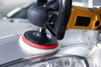 Photo of Man polishing car hood with orbital polisher indoors, closeup