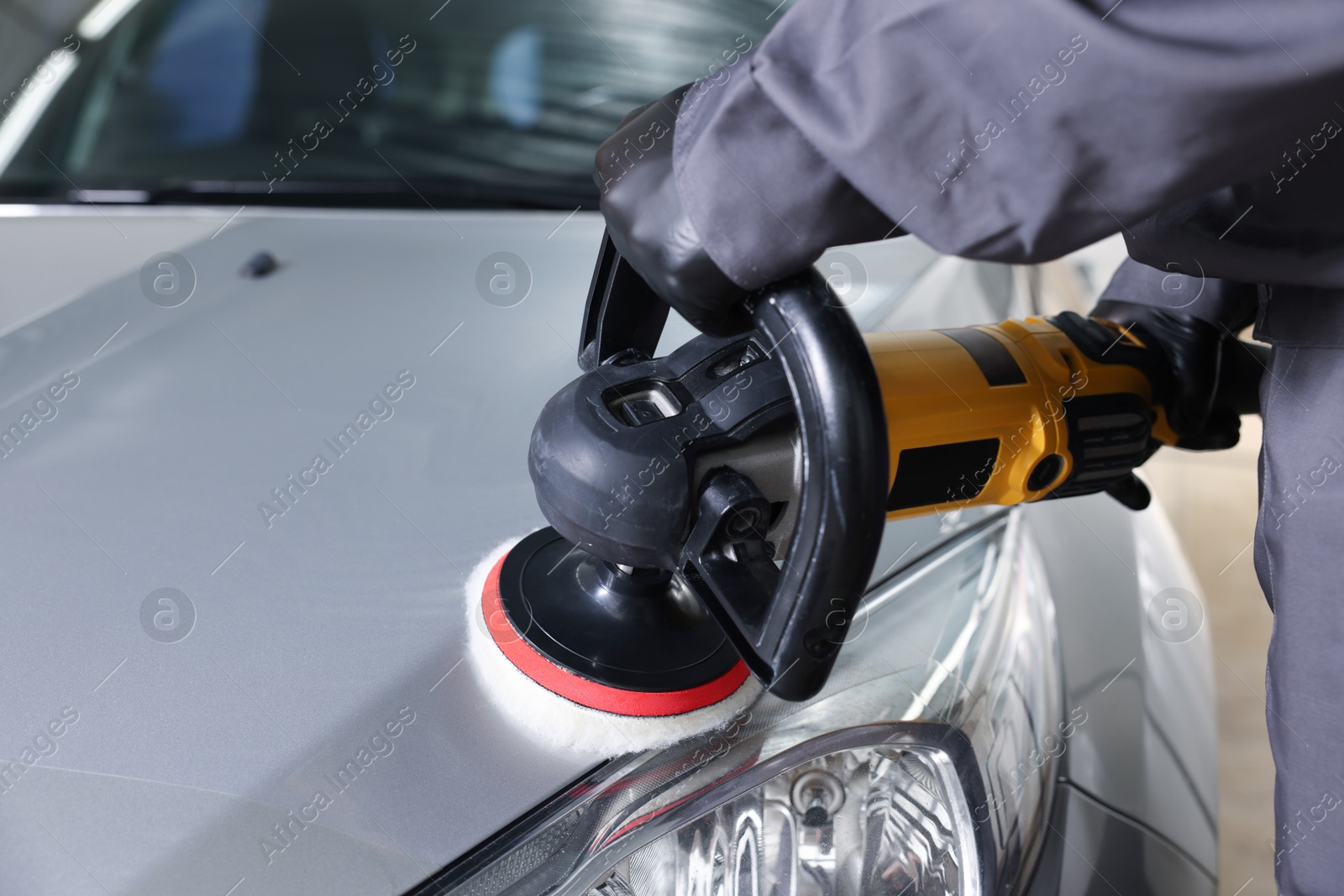 Photo of Man polishing car hood with orbital polisher indoors, closeup