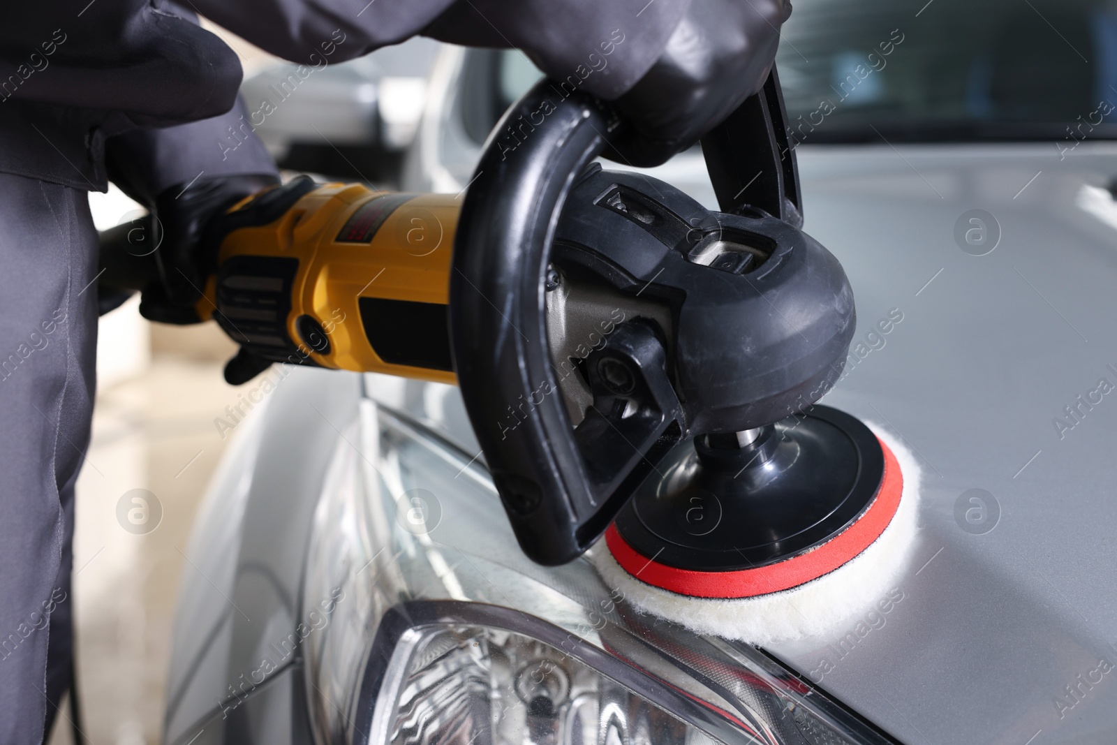 Photo of Man polishing car hood with orbital polisher indoors, closeup