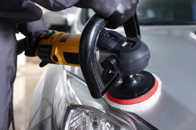 Photo of Man polishing car hood with orbital polisher indoors, closeup