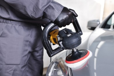 Photo of Man polishing car hood with orbital polisher indoors, closeup