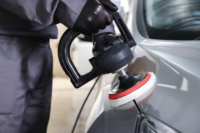 Photo of Man polishing car with orbital polisher indoors, closeup