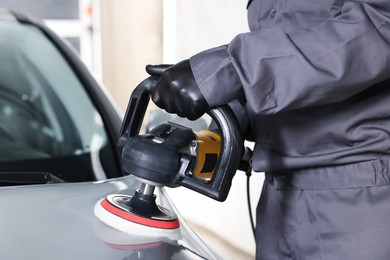 Photo of Man polishing car with orbital polisher indoors, closeup