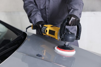 Photo of Man polishing car hood with orbital polisher indoors, closeup