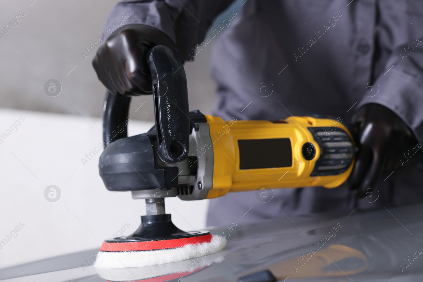 Photo of Man polishing car hood with orbital polisher indoors, closeup