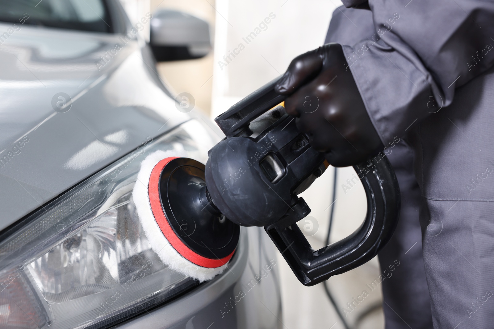 Photo of Man polishing car headlight with orbital polisher indoors, closeup