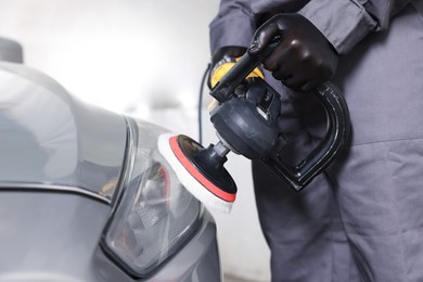 Photo of Man polishing car headlight with orbital polisher indoors, closeup