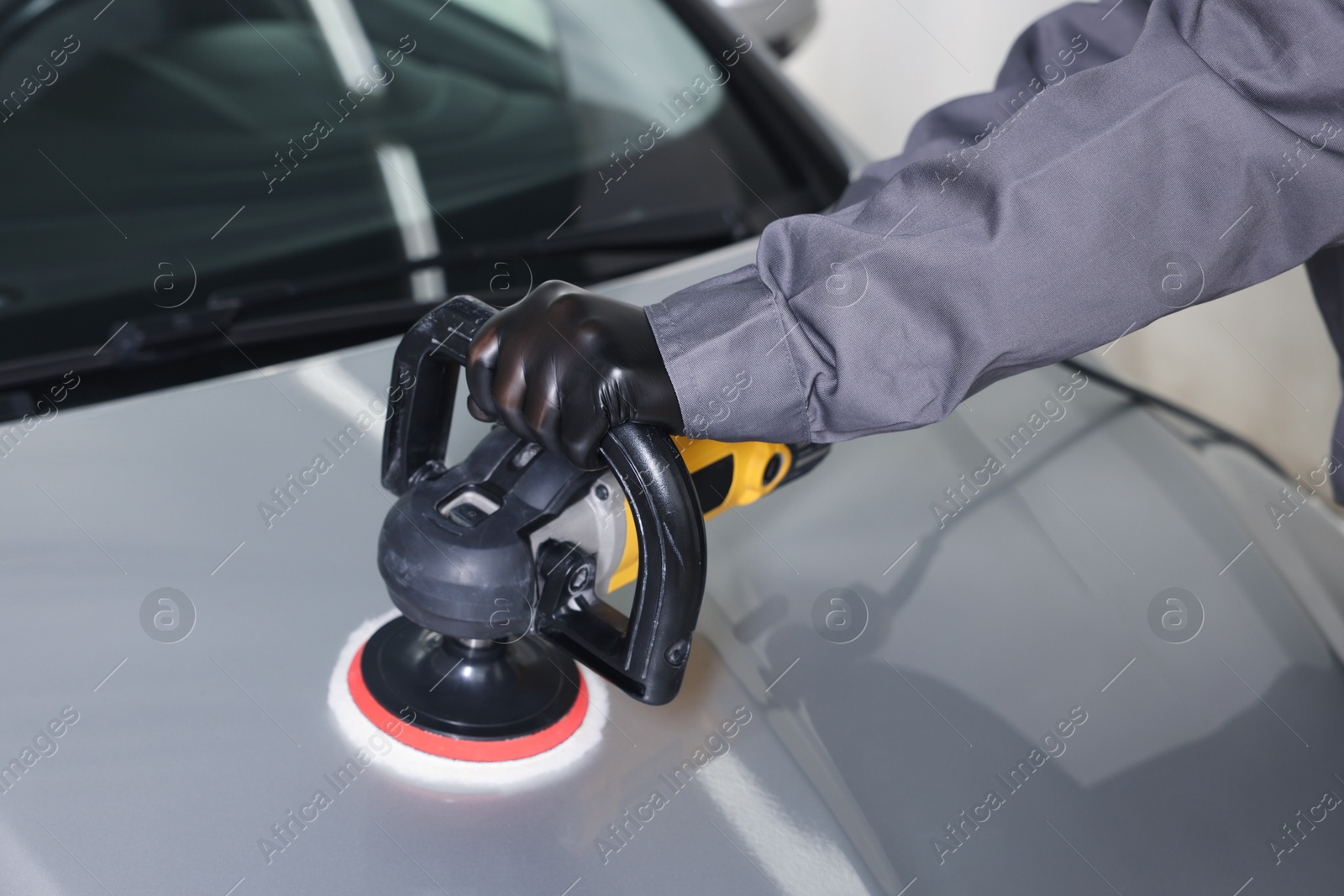 Photo of Man polishing car hood with orbital polisher indoors, closeup