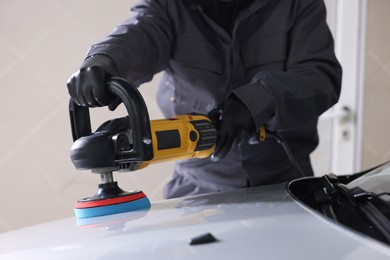 Photo of Man polishing car hood with orbital polisher indoors, closeup