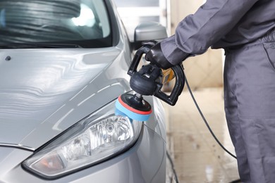 Photo of Man polishing car headlight with orbital polisher indoors, closeup