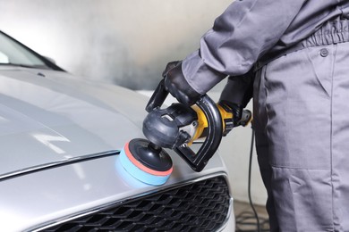 Photo of Man polishing car with orbital polisher indoors, closeup