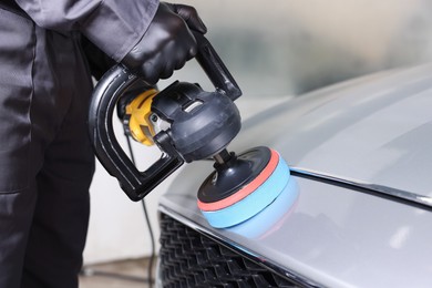 Photo of Man polishing car with orbital polisher indoors, closeup