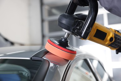 Photo of Man polishing car with orbital polisher indoors, closeup