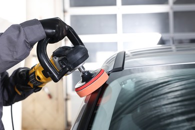 Photo of Man polishing car with orbital polisher indoors, closeup