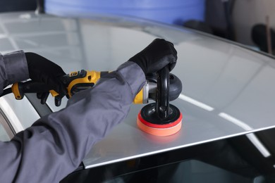 Photo of Man polishing car with orbital polisher indoors, closeup